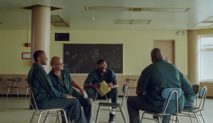 Four incarcerated men sit together in a classroom, smiling.