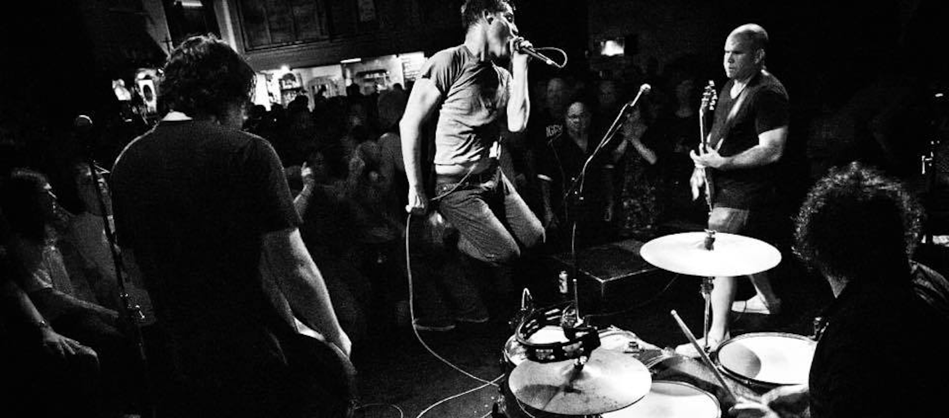 Black and white image of a rock band seen from behind in a packed crowd.