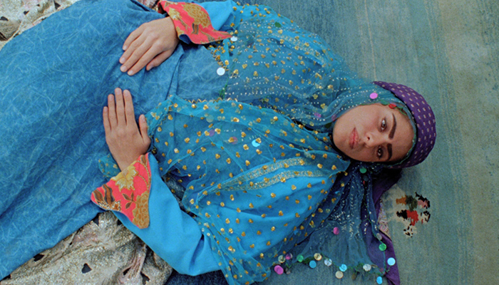 A woman wearing bright blue robes lays on a rug with her hands on her stomach.