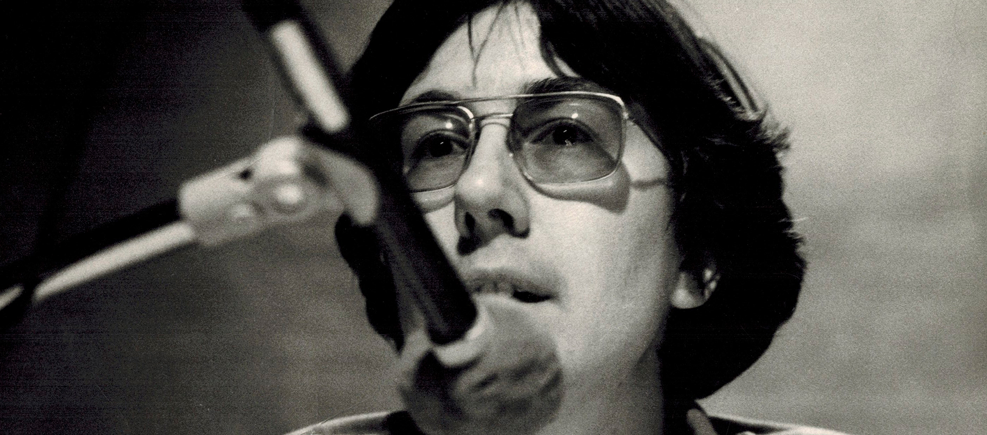 Julia Reichert in the mid 1970s, she has short hair, glasses and is in front of a microphone.