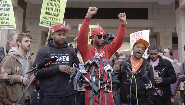 Individuals standing in front of news microphones, the man in the center has his fists raised above his head.