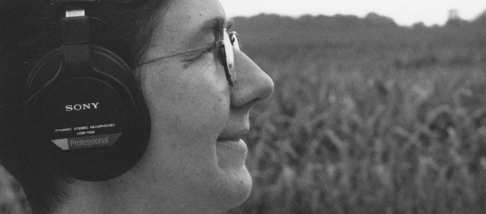 A woman wearing headphones smiles as she looks out onto a field.