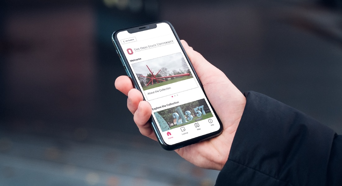 A hand holds a smartphone displaying public art at Ohio State University