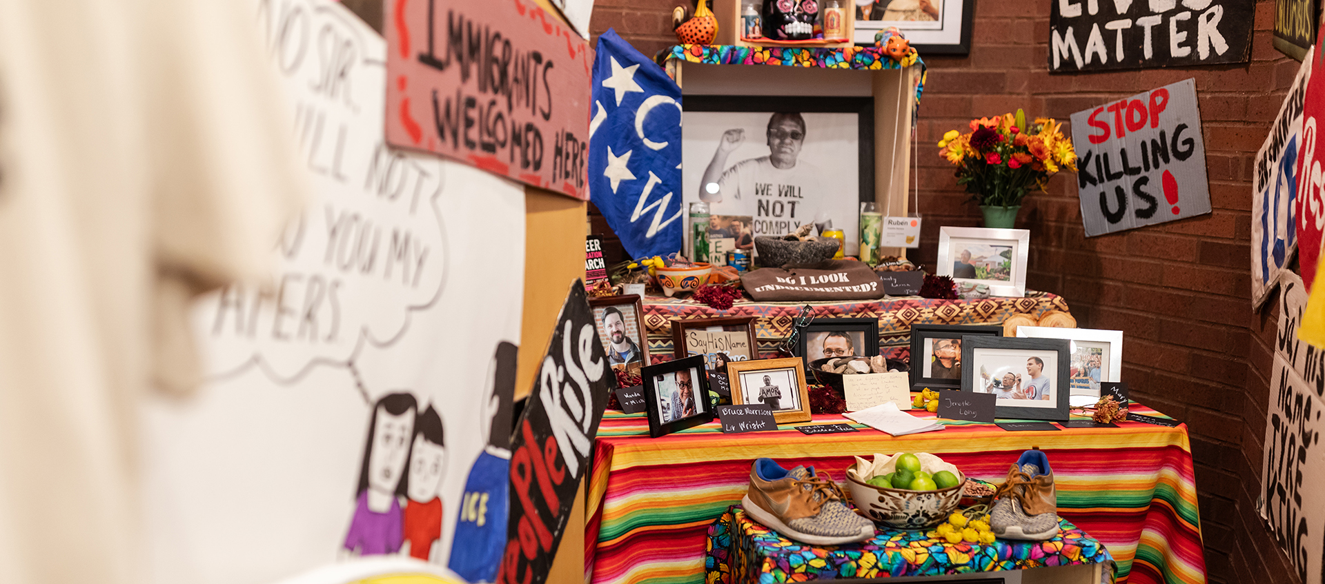 A brightly decorated table altar with framed photos of people, surrounded by signs. 