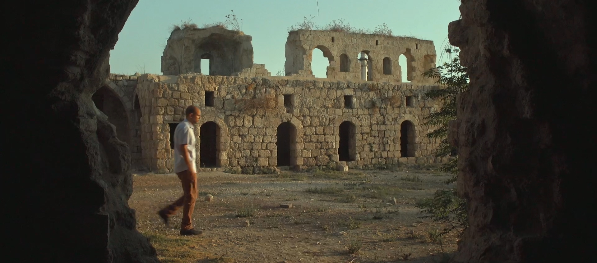 A man walks in front of a stone ruin full of archways.