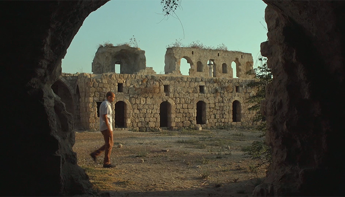 A man walks in front of a stone ruin full of archways.