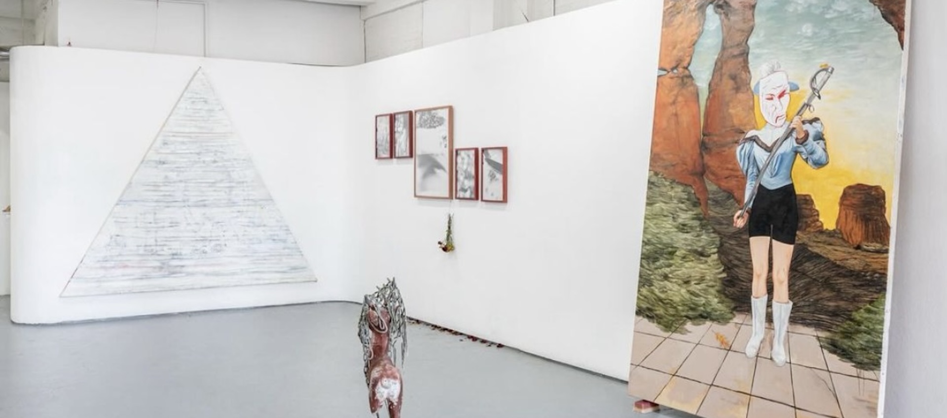 A white-walled gallery space holds a small assortment of works on the walls and a small sculpture on the floor at the center.