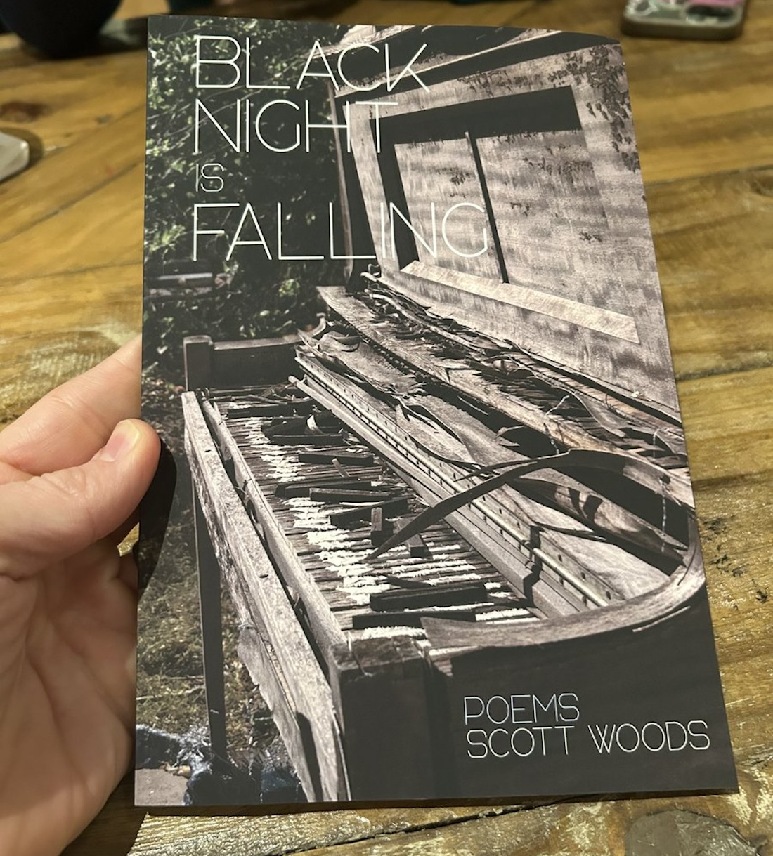 A hand holds a copy of Scott Woods's poetry collection Black Night is Falling.