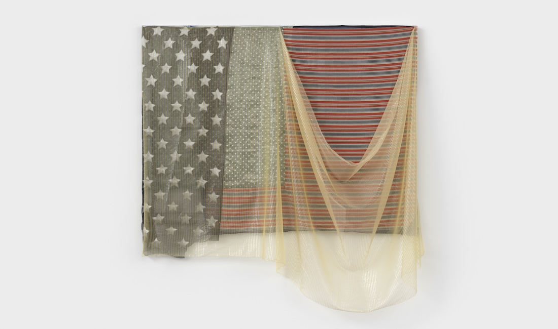 An assemblage of found fabrics suggesting the look of an American flag hangs on a wall.