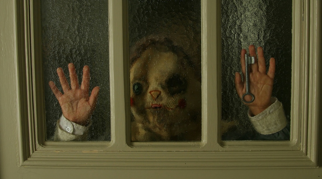 A child wearing a creepy mask presses their face and hands against a window.