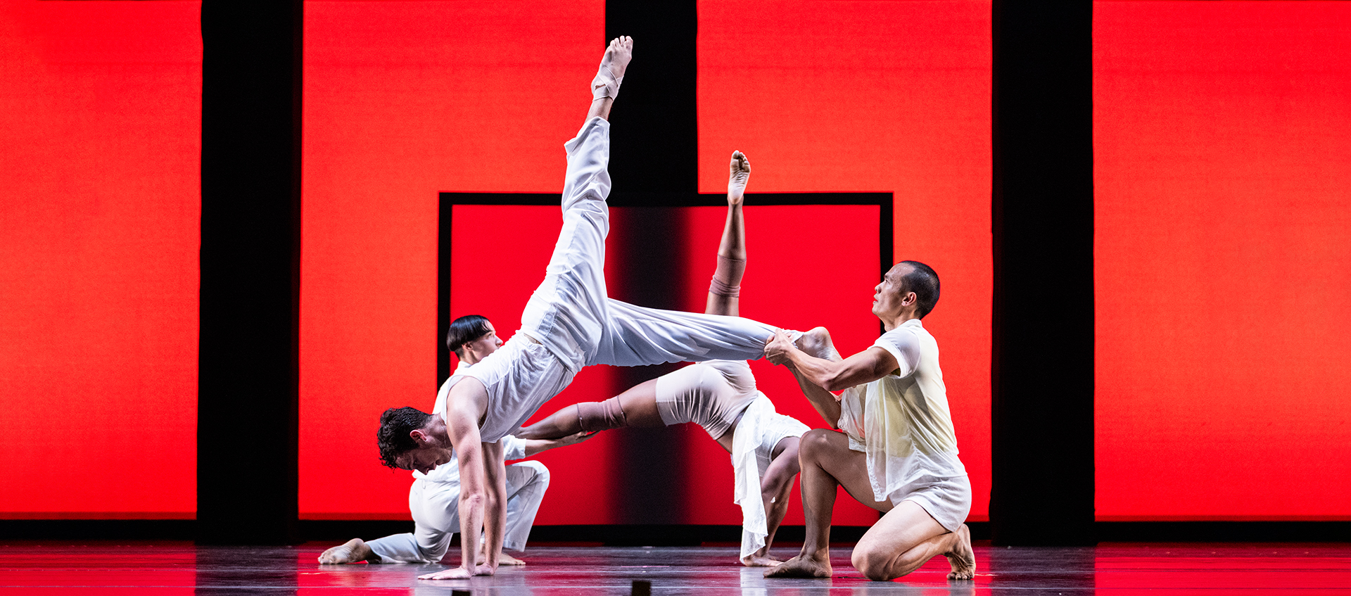 Two dancers in white hold their partners up as they kick their feet in the air.