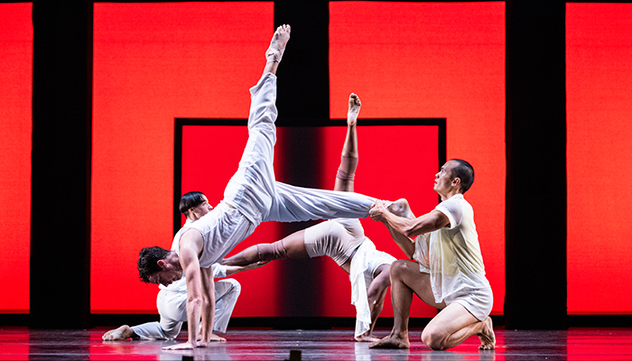 Two dancers in white hold their partners up as they kick their feet in the air.