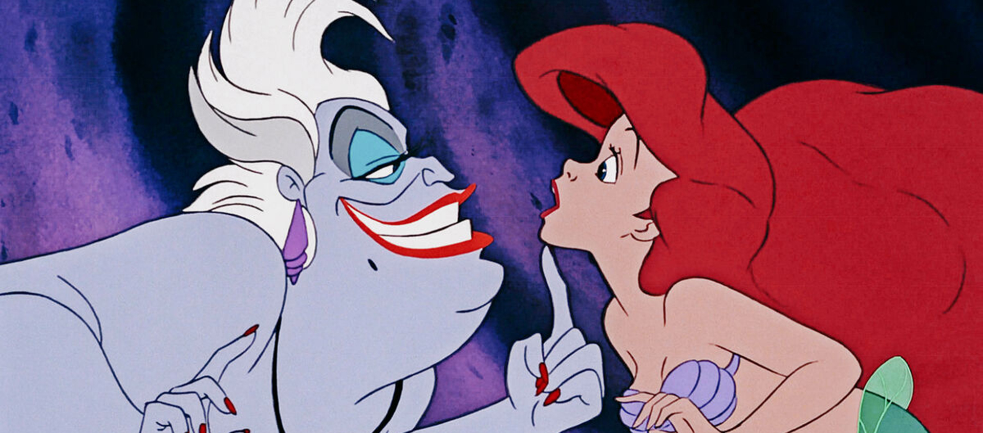 The purple-skinned sea witch Ursula tickles mermaid Ariel’s chin. Ariel has bright red hair.
