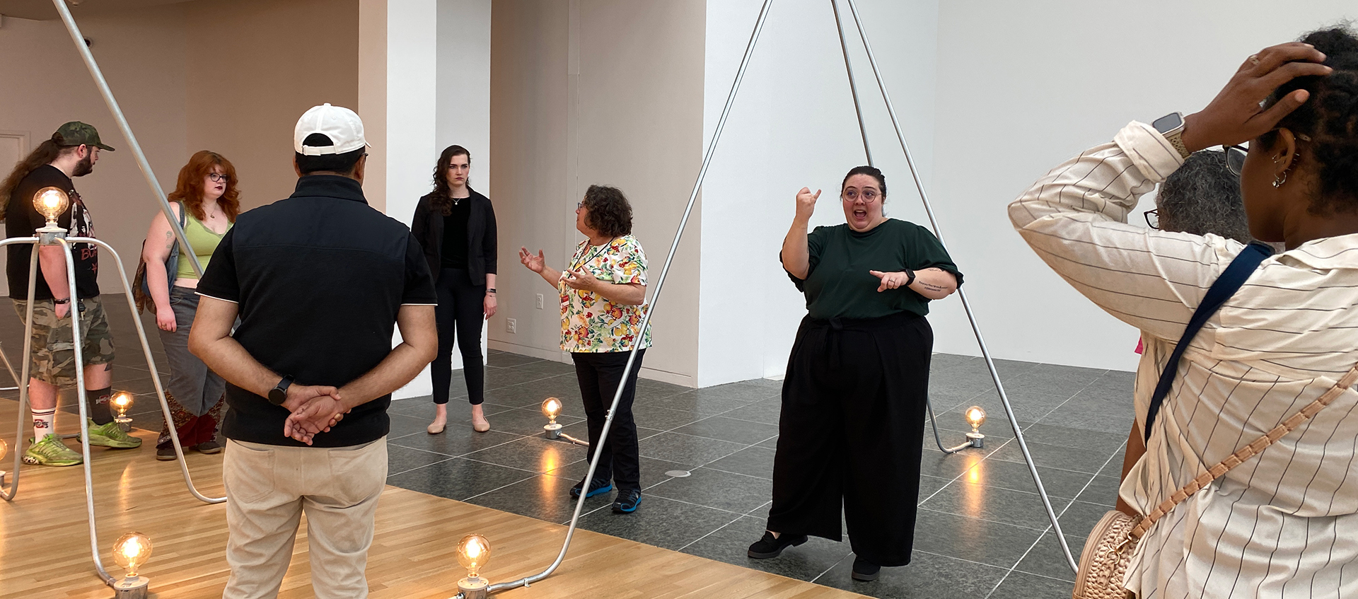 A group of people gather around an ASL interpreter in a gallery space featuring artwork from Nancy Holt: Power Systems.