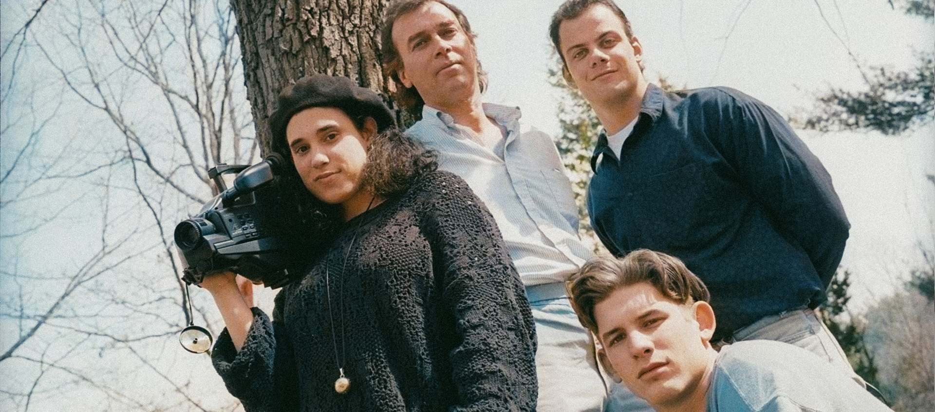 Three teens and one adult pose for a photo in front of a tree. The young woman holds a camera.