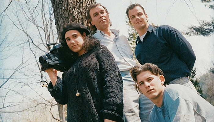 Three teens and one adult pose for a photo in front of a tree. The young woman holds a camera.