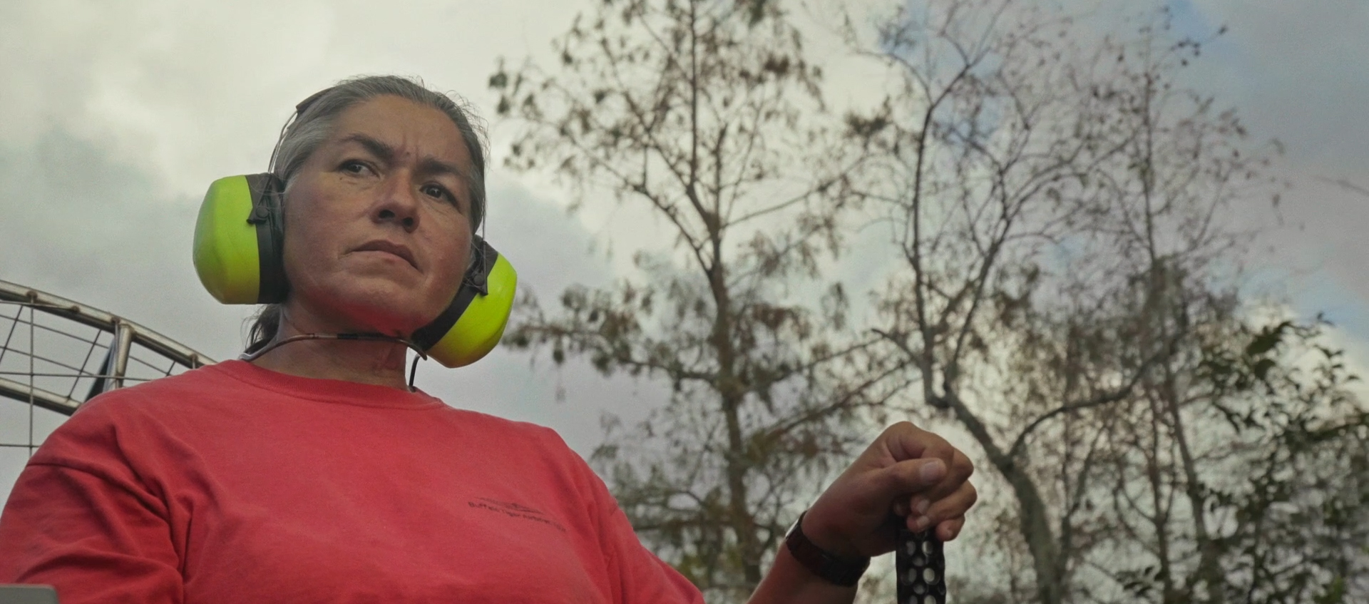 A woman wearing headphones looks beyond the camera intently as she drives a boat outside of view.