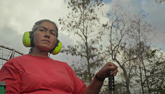 A woman wearing headphones looks beyond the camera intently as she drives a boat outside of view.