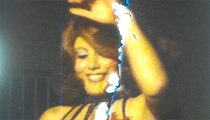 A distorted archival image of an Iranian woman smiling and raising her hand.