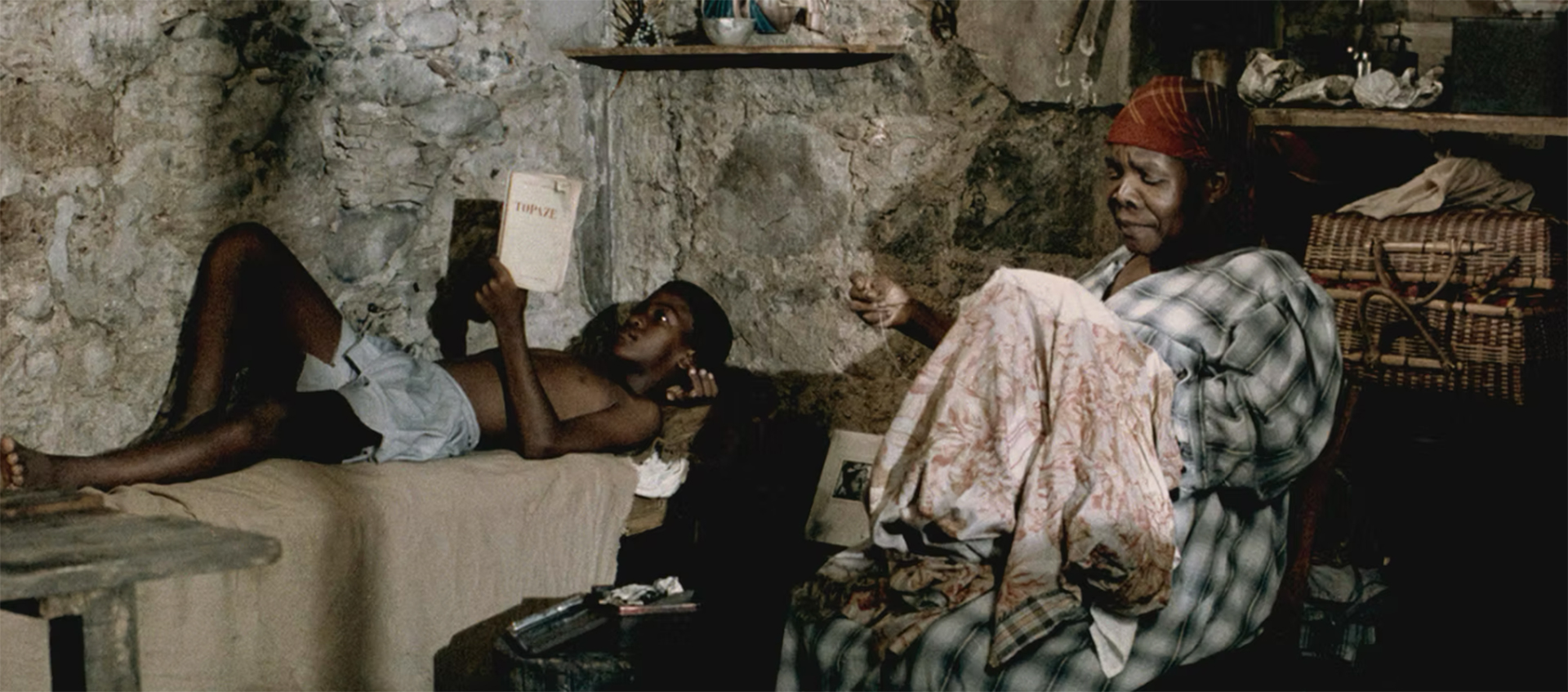 An old woman sewing and a child laying down are in a small room.