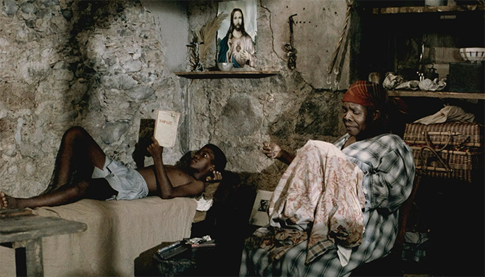 An old woman sewing and a child laying down are in a small room.