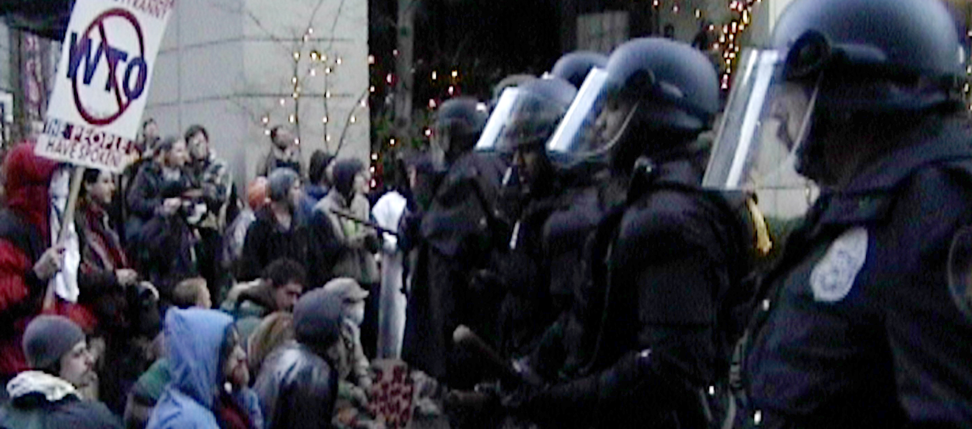 Police in riot gear face off with protesters in the street.
