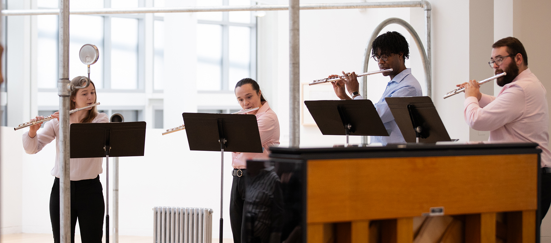  Four students with music stands play flutes amid silver pipes from an art installation by Nancy Holt. A piano is in the foreground.