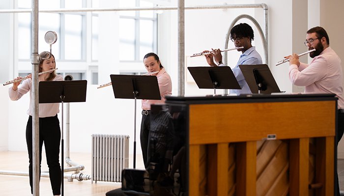  Four students with music stands play flutes amid silver pipes from an art installation by Nancy Holt. A piano is in the foreground.