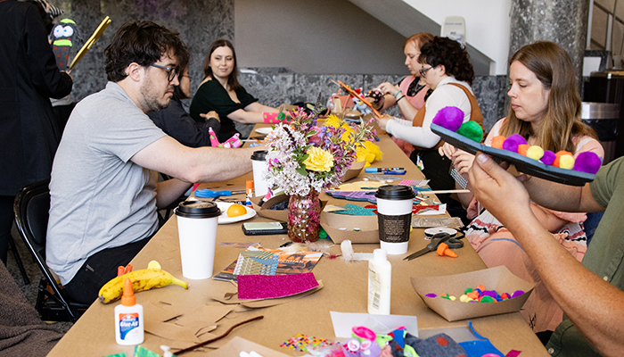 People sit at a long table filled with art and craft supplies. Each person works on creating their own artwork.