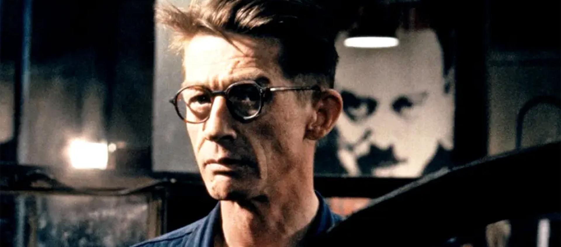 A still of John Hurt as Winston Smith in 1984. A black-and-white face is behind him.