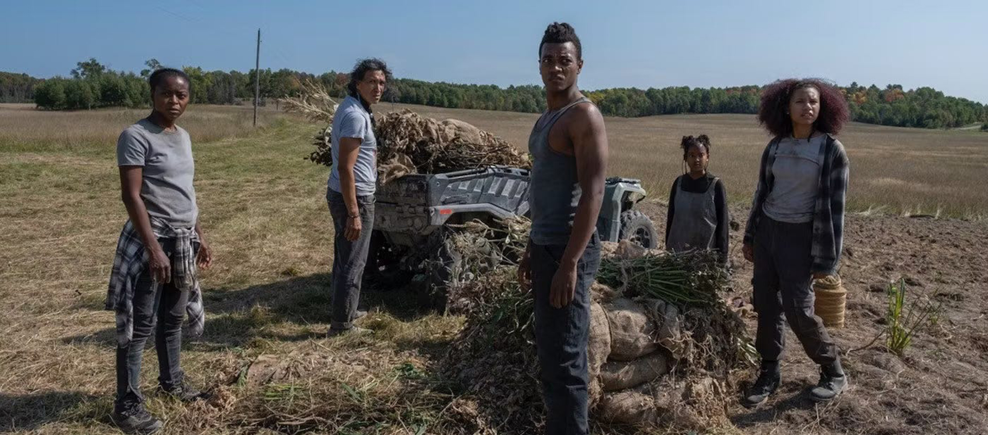 A Black and Native American family stands in a field looking into the distance.