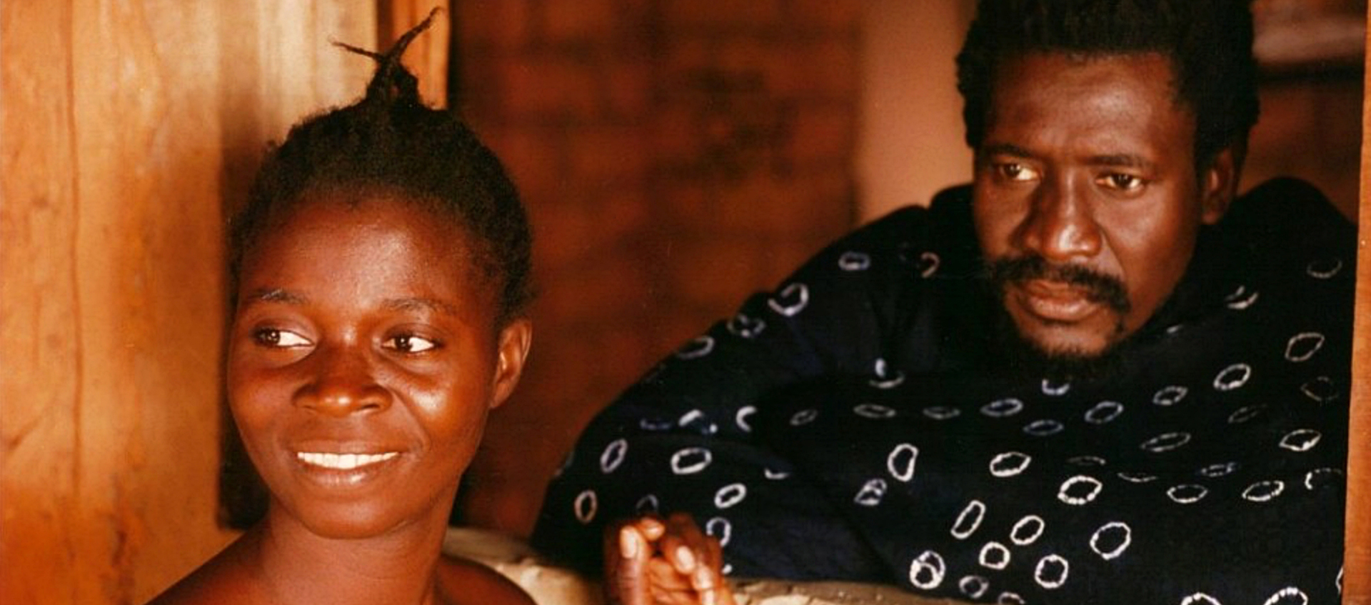 A still of a Black woman and a Black man. The Black woman smiles. The Black man wears a serious expression.