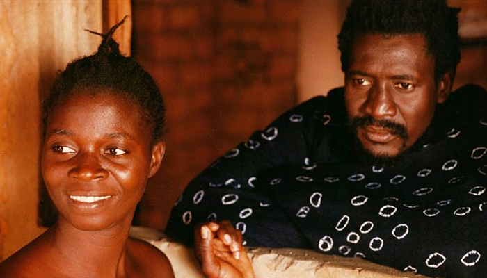 A still of a Black woman and a Black man. The Black woman smiles. The Black man wears a serious expression.