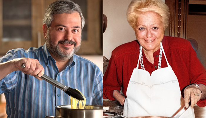 A man holds up pasta with a pair of tongs and a woman wearing an apron stirs a pot.