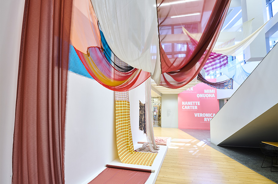 A colorful installation of fabrics hanging from the ceiling and walls of the Wexner Center lobby.