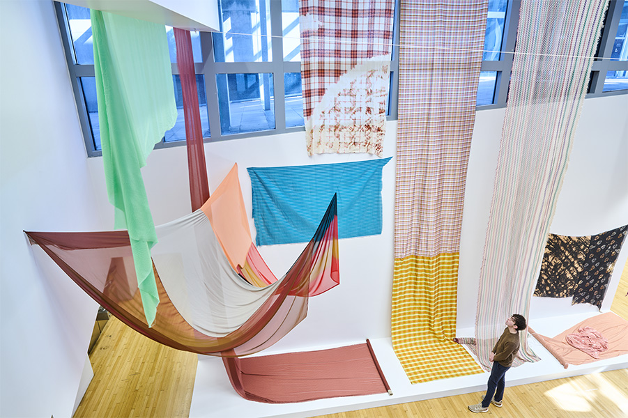 A colorful installation of fabrics hanging from the ceiling and walls of the Wexner Center lobby.