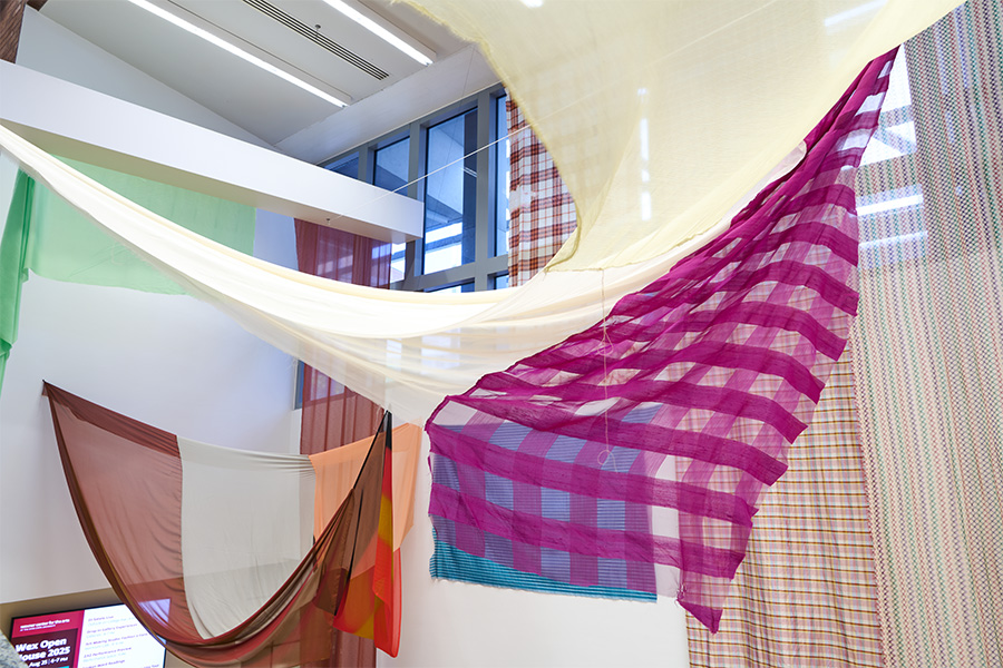 A colorful installation of fabrics hanging from the ceiling and walls of the Wexner Center lobby.