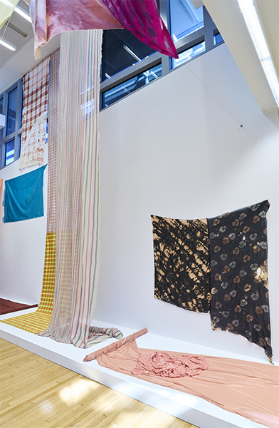 A colorful fabric installation in the Wexner Center lobby. Some fabric lies on a platform. Others are draped from the ceiling.