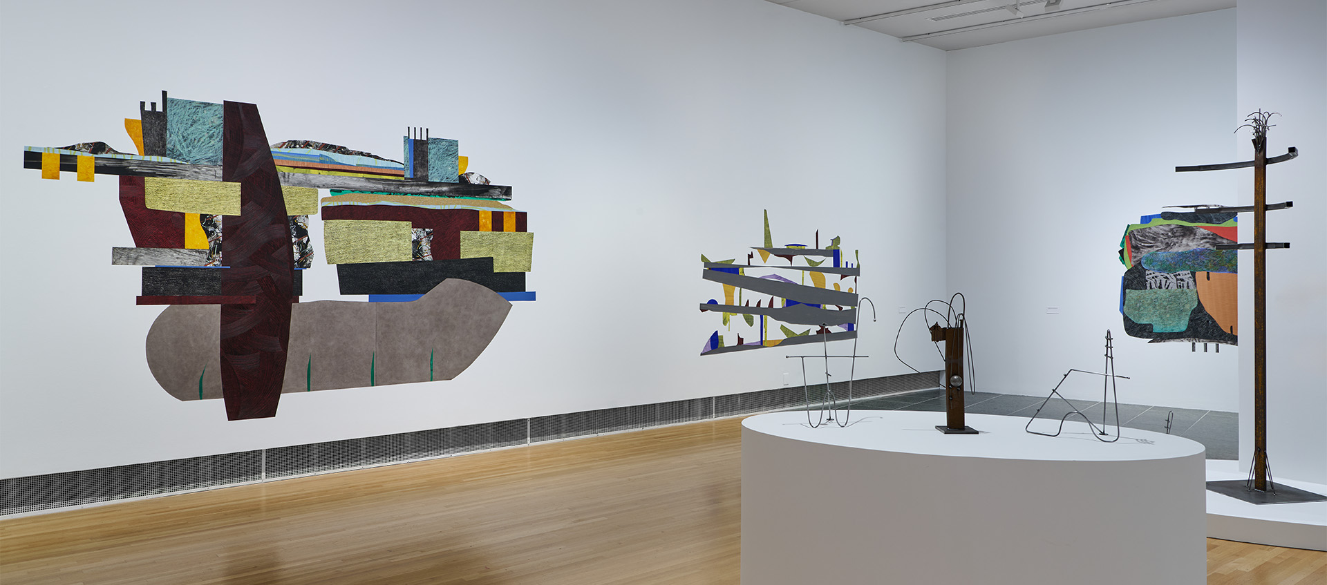 A gallery space featuring colorful works made of Mylar on the white walls and metal sculptures on platforms.