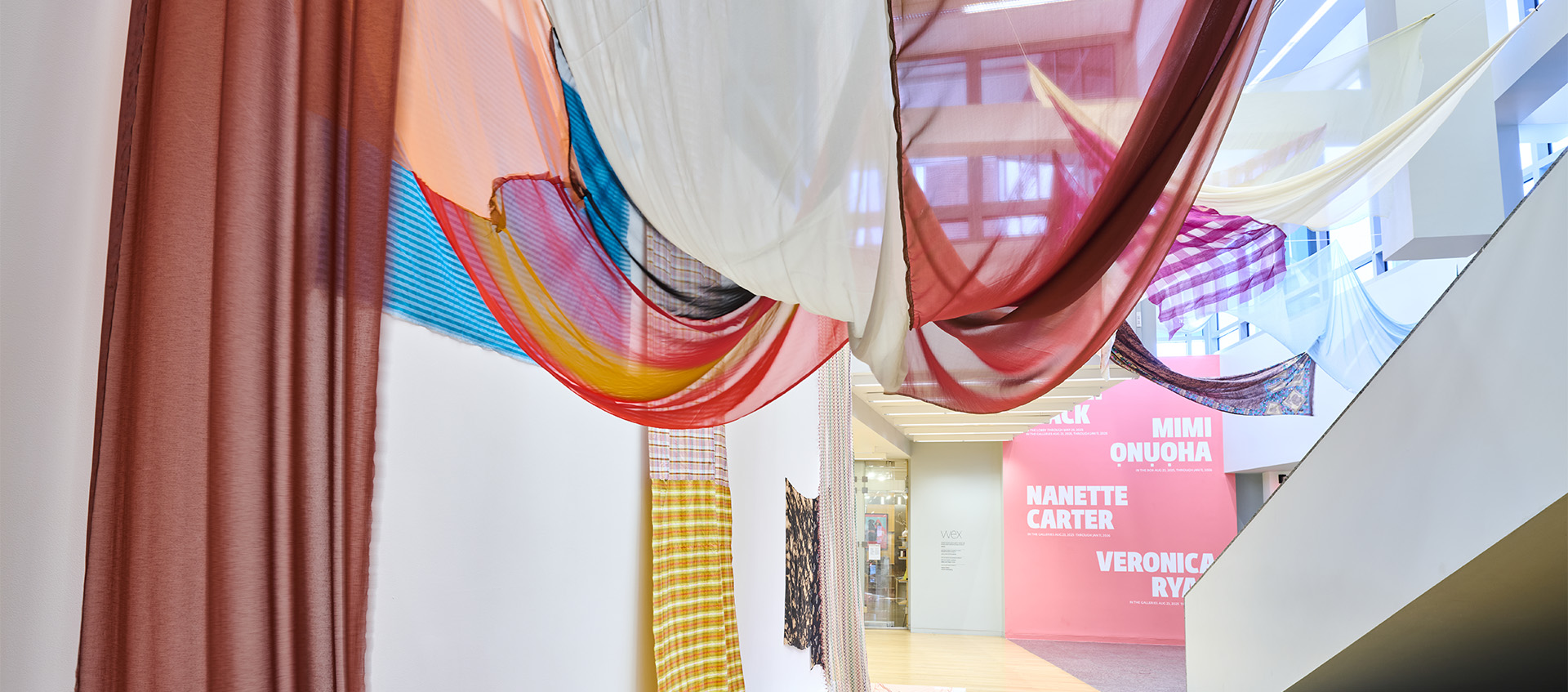 A colorful installation of fabrics hanging from the ceiling and walls of the Wexner Center lobby.