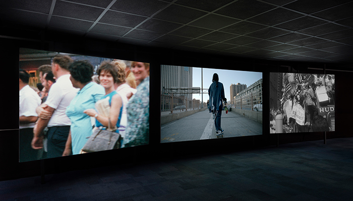 Three large screens project images in a dark room.