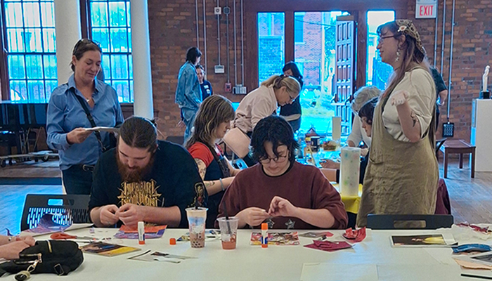 A group of people sit and stand around tables while making art.