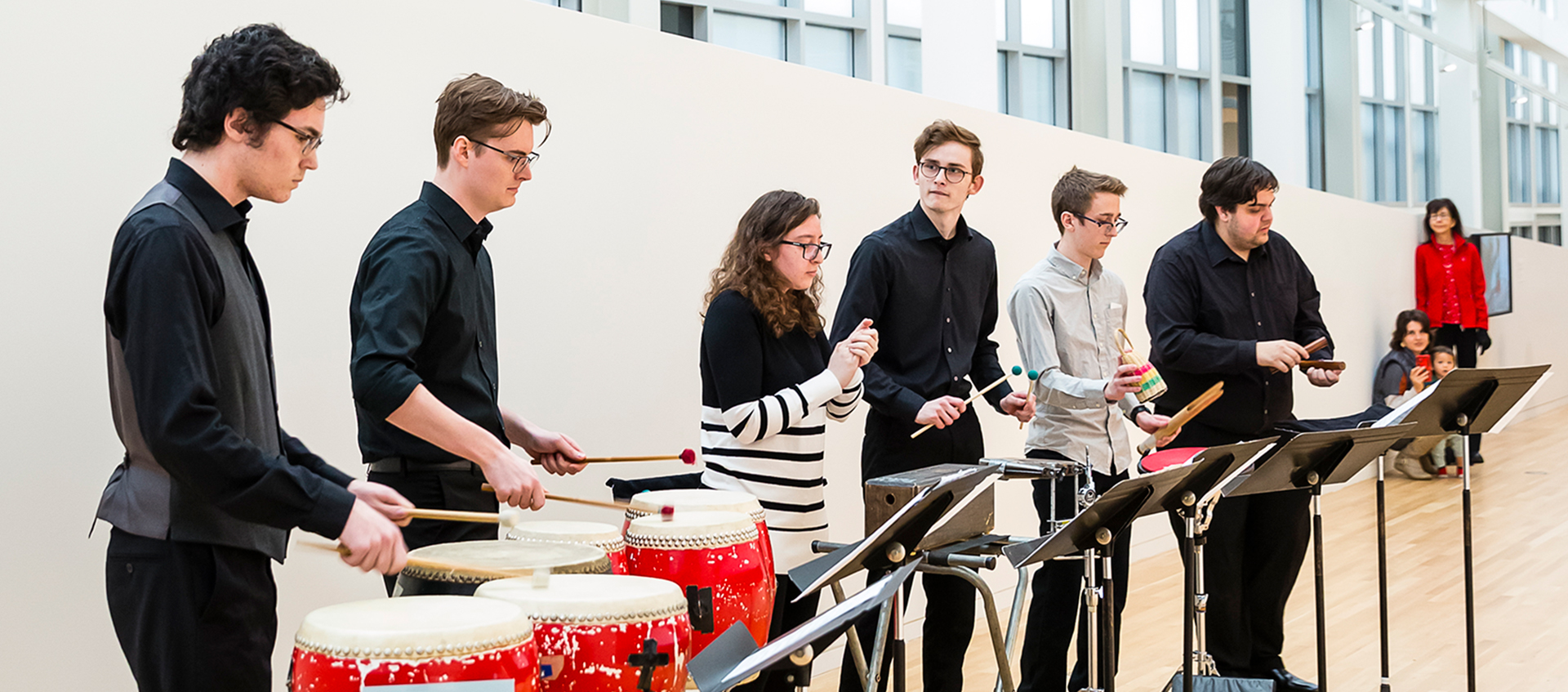 Six percussionists play a variety of instruments in a gallery setting. 