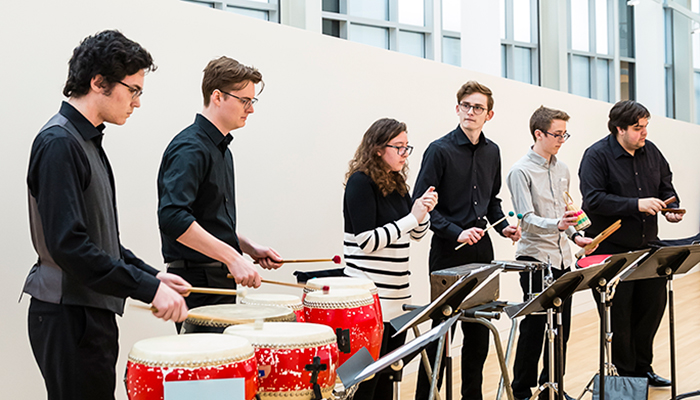 Six percussionists play a variety of instruments in a gallery setting. 