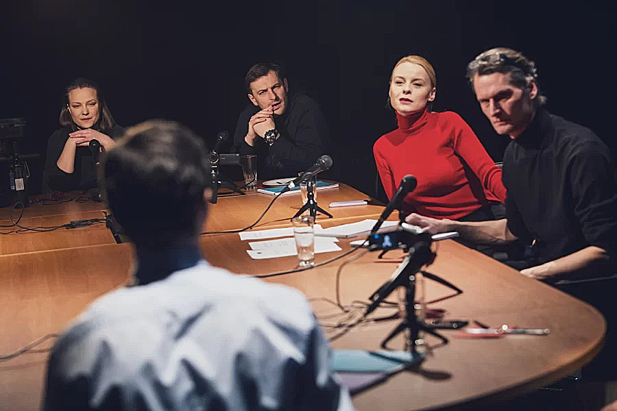 Five people sit around a table with video cameras and microphones on it. 