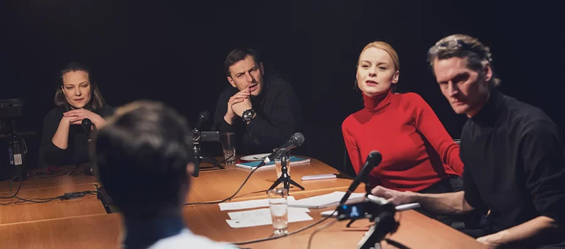 Five people sit around a table with video cameras and microphones on it. 