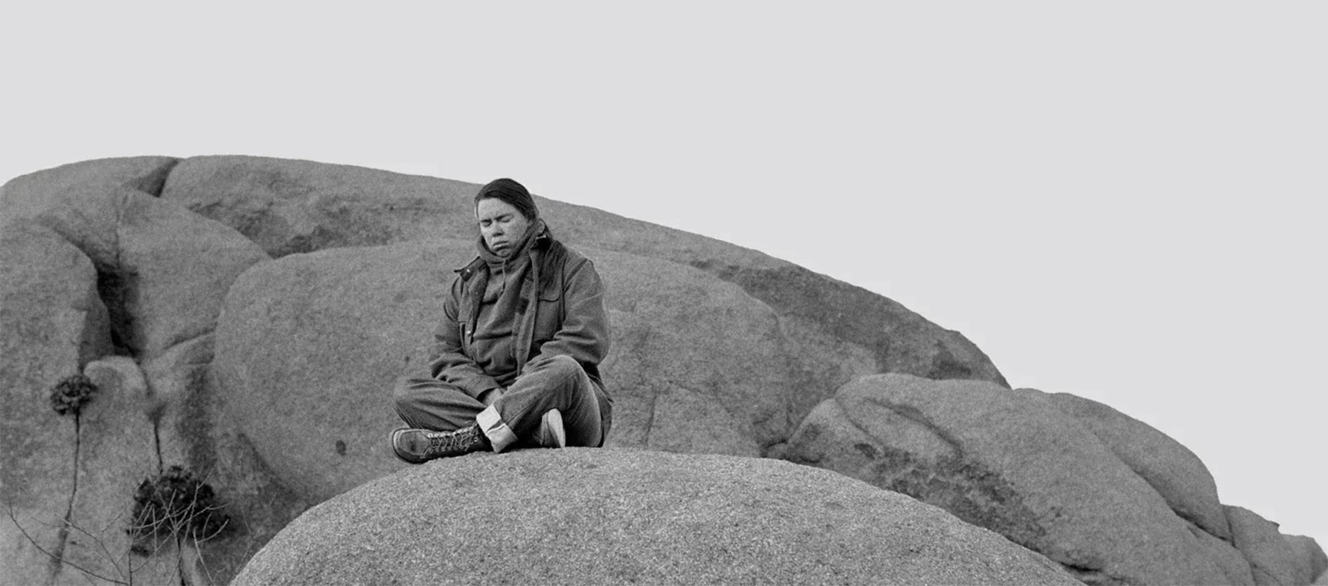 A woman sits crosslegged on top of a boulder with her eyes closed.