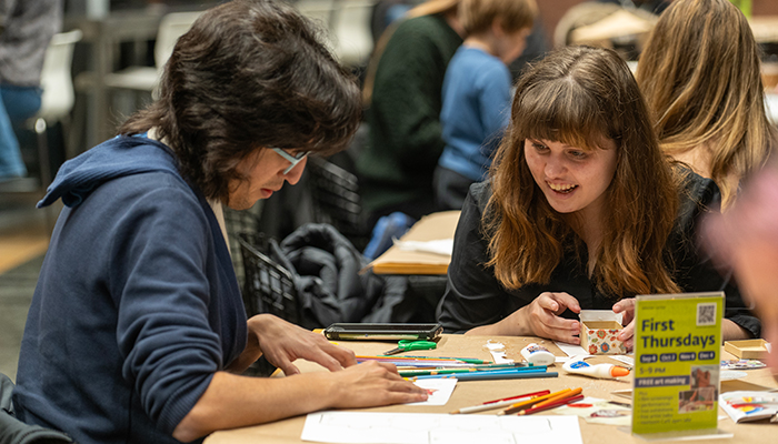 Two people sit at a table in Heirloom Café and make art. More people sit in the background.