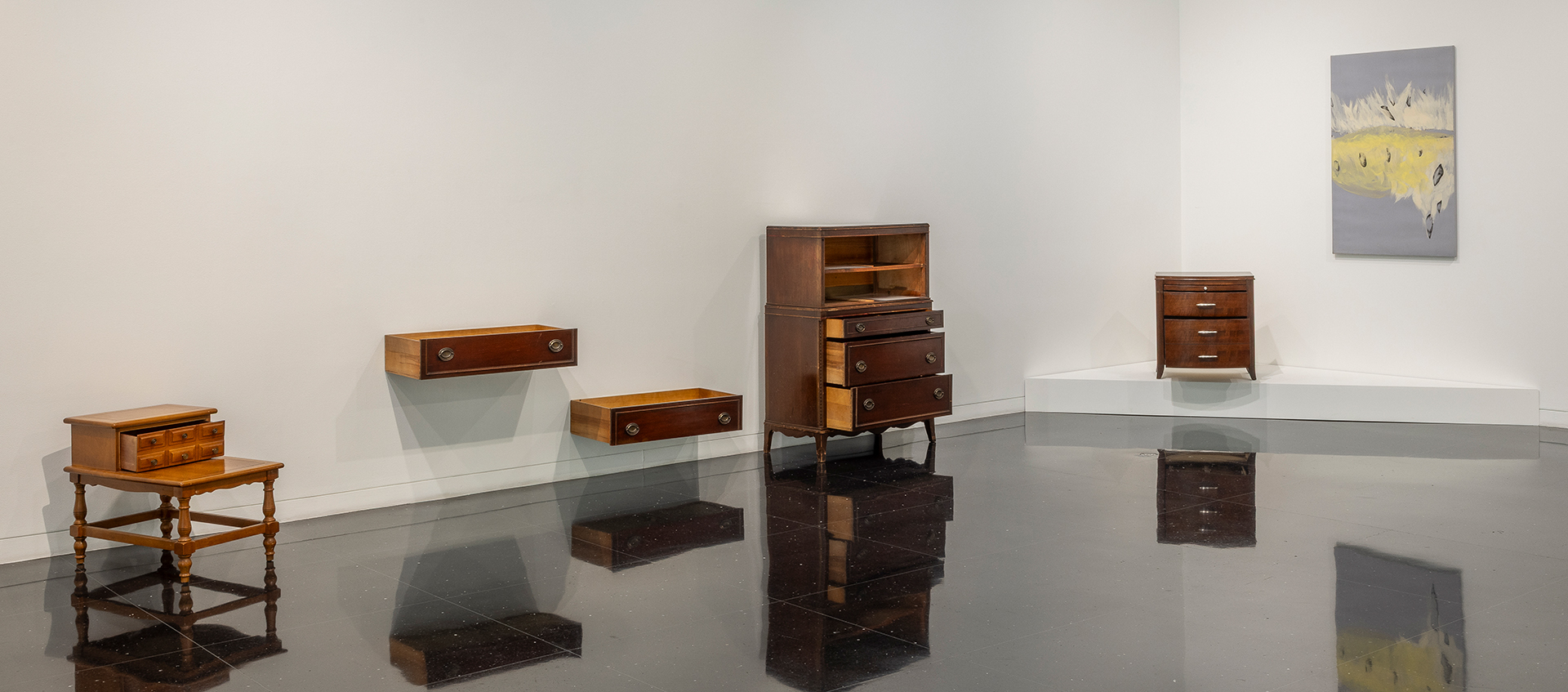 A gallery with a reflective floor displays antique furniture with partially opened doors and drawers. An abstract gray, white, and yellow painting hangs nearby. 