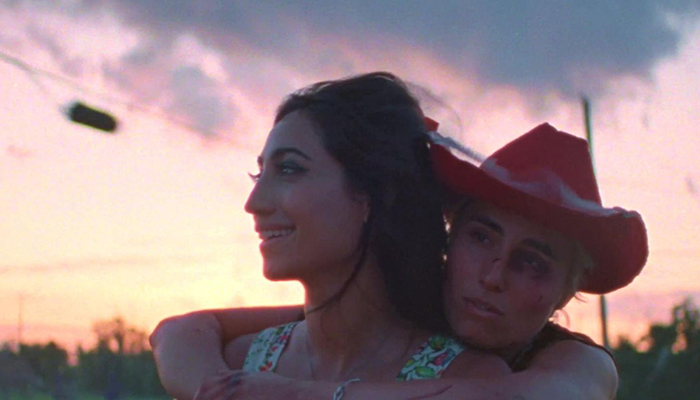 At dusk a woman wearing a red cowboy at wraps her arms around another woman's shoulders.